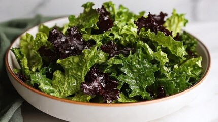 A white bowl with a brown rim holds a fresh salad of green and red lettuce leaves.