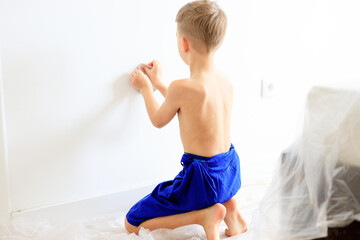 A young boy renovating a room, sanding the walls with sandpaper and painting them white with a...