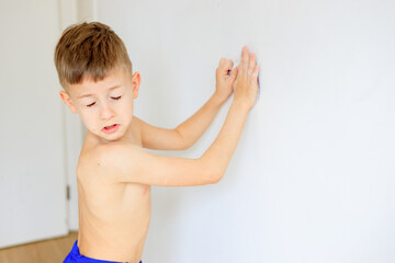 A young boy renovating a room, sanding the walls with sandpaper and painting them white with a...