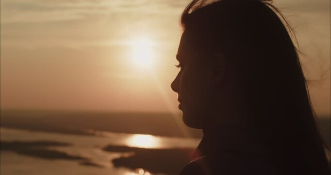 Young woman watching golden sunset over river landscape