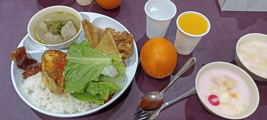 Plated Meal with Assorted Food and Refreshments. A colorful dish of rice, meat, vegetables, and soup, served with fresh fruit, orange juice, and a creamy fruit dessert, displayed on a table