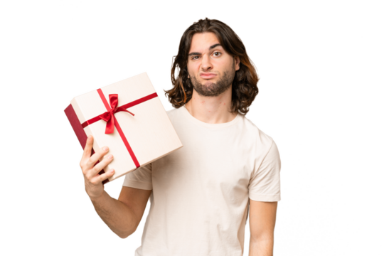 Young handsome man holding a gift over isolated background with sad expression