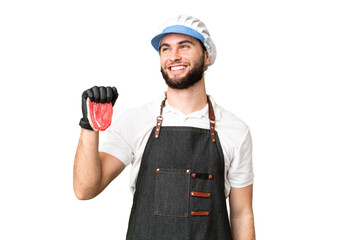 Butcher man wearing an apron and serving fresh cut meat over isolated chroma key background thinking an idea while looking up