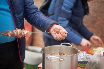 Man cooks meat on street. Planting meat on blade. Bonfire with food.