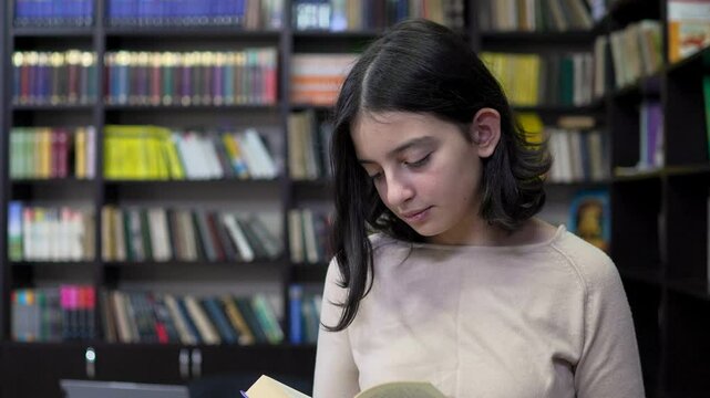 Teenage student girl reading a book in the library