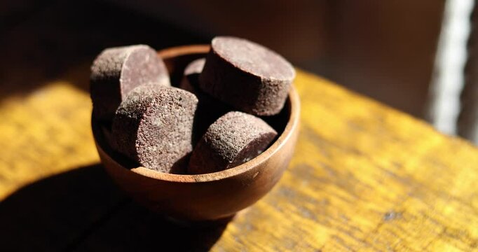 Close-up view of a small, dark-brown wooden bowl filled with several irregularly shaped pieces of dark, possibly chocolate-like material. 