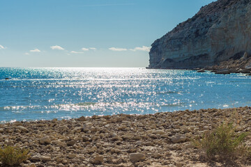 Tranquil Sandy Beach with Clear Blue Water and Cliff Background