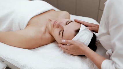 Young professional woman cosmetologist doing skin care facial treatment examining its condition for female client in beauty clinic. Cosmetology and beauty procedure concept