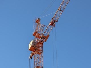 Equipment for the construction and lifting of bulky goods with construction materials. A tower crane on a construction site against a blue sky background. Construction equipment.