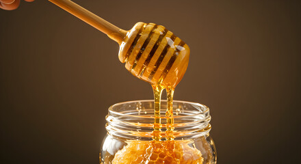 Golden Honey Dripping From Dipper Into Glass Jar Full Of Honeycomb