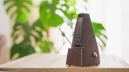 Vintage metronome ticking on wooden table with green foliage background