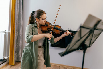 Violin student playing notes at home, preparing for a future performance. A young musician sharpens her violin skills during an intensive rehearsal © Irina_Evva