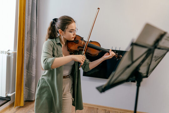 Violin student playing notes at home, preparing for a future performance. A young musician sharpens her violin skills during an intensive rehearsal