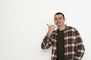 A man stands indoors smiling and giving a thumbs up gesture. He is dressed in a checked flannel...