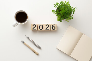 2026 wooden blocks with coffee, notebook, pens, and potted plant on white minimalist desk, flat lay for productivity, planning, and New Year workspace concept