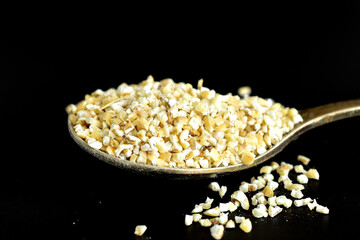 Yellow barley groats lie on a metal spoon.
