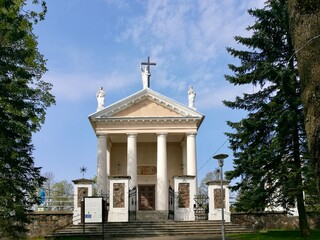 Exaltation of Holy Cross church in Taujenai. Rural church Neoclassical church with a triangular pediment adorned with statues. Four tall white columns support the portico. 
