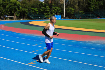 Senior Asian athlete is practicing running in the professional blue track for professional exercise, sport training workout and healthy for longevity concept