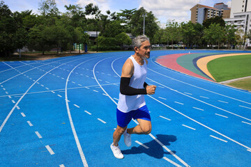 Senior Asian athlete is practicing running in the professional blue track for professional...
