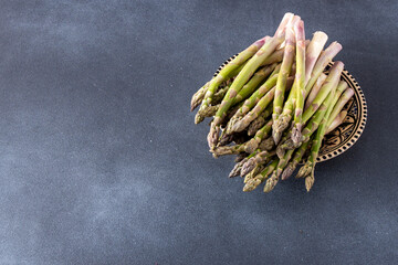 Green asparagus in plate on dark background. Vegetable sprouts stems. Fresh food bowl top view. Copy space.