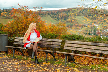 Beautiful long hair woman sits on the bench in the park on a warm day in autumn