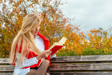 Beautiful young woman reading a book on a park bench in an autumn scenery