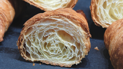 Fototapeta premium A piece of croissant is cut in half. The other half is not visible. The croissant is on a black surface