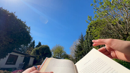 Reading a book in the garden on a warm summer day with blue sky and sun shining, POV, low angle