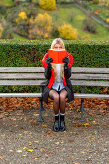Woman sits in the park, reading a book on a warm day of autumn
