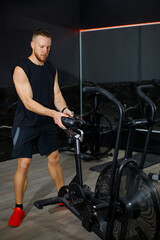 Athletic young man adjusting stationary exercise bike in gym