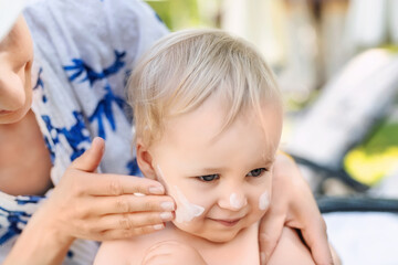 Mother applying sunscreen protection creme on cute little toddler boy face. Mom using sunblocking...