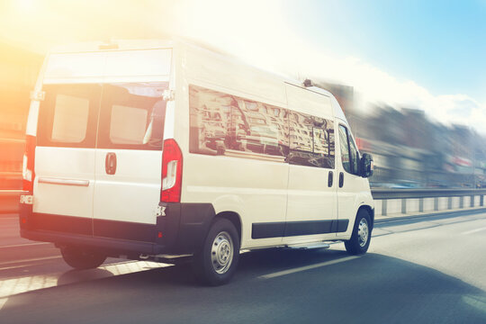 Unrecognizable small passenger van hurry up on highway at city street traffic with urban cityscape and sunset sky on background. Charter or shuttle bus  van hurry up on road with motion blur effect