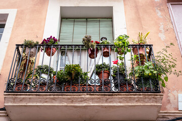 A quaint balcony with a variety of potted plants and flowers set against a faded pink facade with a...