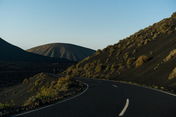 A road leading to volcano on a volcanic island, under a blue sky dotted with clouds. Lanzarote	