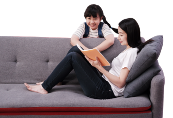 Smiling Asian mother teaching daughter for reading a book on sofa at home together. Child educational for homeschooling concept