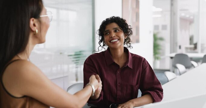 Indian business professional woman shaking hands with Kazakh female colleague or business partner after successful negotiation, smiling, thanking for consultation, deal, partnership, finish meeting