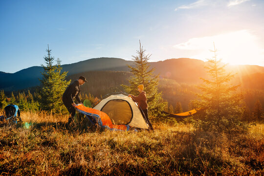 Tourists pitch tourist tent in camp in mountains at sunset. Family recreation in nature.