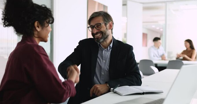 Smiling Latino businessman dressed in suit shaking hands with young Indian woman, accomplish business meeting or negotiations, establish partnership, conclude agreement, make business profitable deal