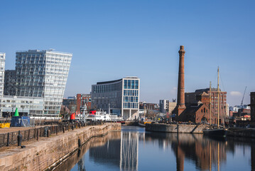 View of Liverpool's waterfront featuring Albert Dock, the Pump House chimney, and modern glass buildings reflected in calm water.