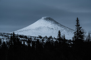 Majestic snow-covered mountain rises above winter forest in Sweden's serene landscape