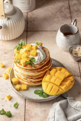 Pancakes with mango, whipped cream and honey on plate on beige tile background. Delicious dessert for Maslenitsa or Pancake Day. Healthy breakfast