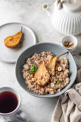 Wholegrain oatmeal porridge with caramelized pear, nuts and honey on white table, healthy food for breakfast