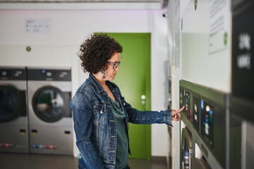 Woman using washing machine touchscreen at laundromat during daily laundry routine