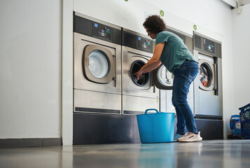 Woman placing laundry into dryer at laundromat with blue basket