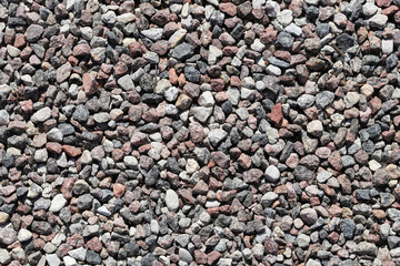 Colorful gravel texture. Small stones background. Construction material. Rough surface detail. Natural crushed rock. Stone wall pattern. Outdoor pavement ground. Gray red mix.