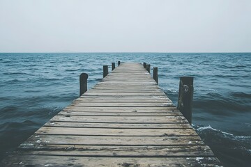 Wooden pier stretches into calm ocean under a cloudy sky.