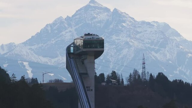 Aerial view of the Bergisel Ski Jump in Innsbruck, Austria, with gradual motion showcasing its modern design and the surrounding snow capped Alps.