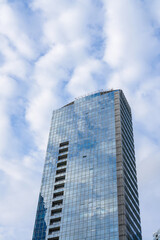 Fototapeta premium Looking Up at Modern Glass Skyscraper with Sky Reflection and Clouds