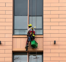 Window cleaner working on a glass facade modern skyscraper. An industrial mountaineering worker washes the glass windows of a high-rise building. A man window cleaner washes the facade of a building.	
