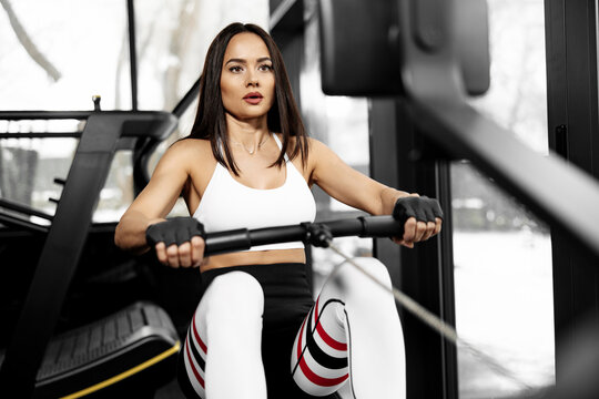 Close-up photo of energic young woman exercising on a rowing machine at the gym